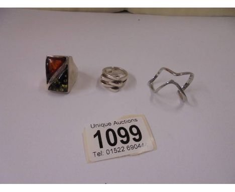 A silver ring set orange and green amber, another silver ring and an un-marked ring.