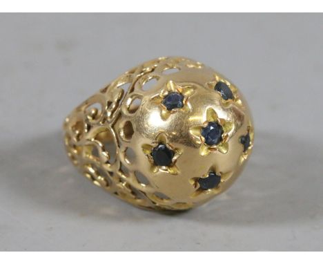A yellow metal dome topped ring with pierced scrollwork shoulders and set with six sapphires, size k 1/2.