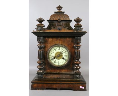 A 19th century carved walnut eight day mantel clock with turned supports, enamel chapter ring and striking on a gong.