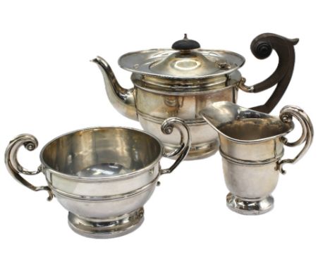 A matched Edwardian silver three piece tea set, all of circular shape with ornate scrolled handles, upon circular feet, tea p
