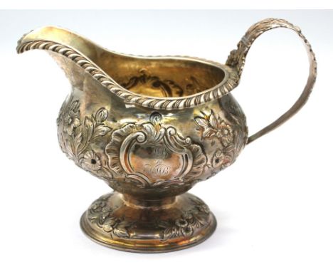 A William IV silver cream jug, with embossed floral and foliage design upon a circular foot, with gilt interior and foliate c
