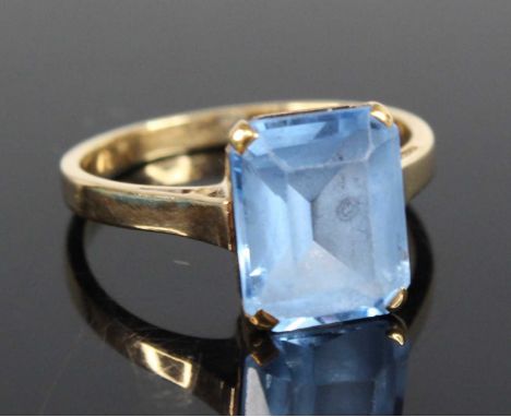 A yellow metal synthetic spinel single stone ring, comprising a rectangular cut synthetic blue spinel in a four-claw setting,