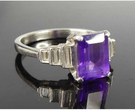 An Art Deco style platinum, amethyst and diamond dress ring, the four claw set emerald cut amethyst measuring approx. 8.1x5.9