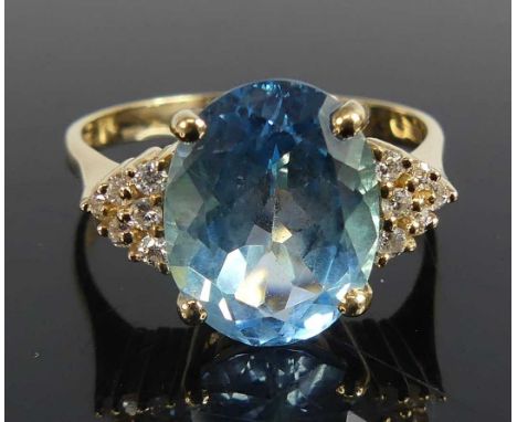 A yellow metal blue topaz and diamond set dress ring comprising a centre oval blue topaz with 6 melee cut diamonds to either 