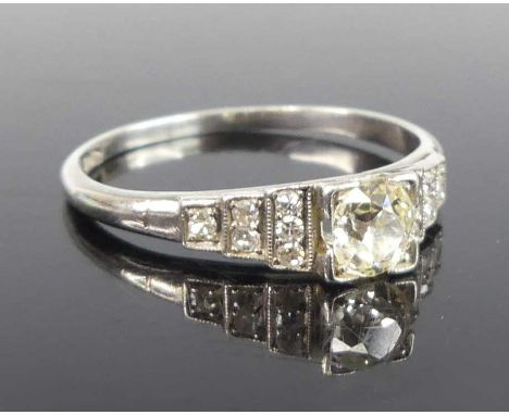 An Art Deco platinum and diamond dress ring, arranged as a centre old round cut diamond measuring 0.45 carats, colour tinted,