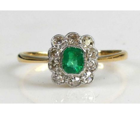 A yellow and white metal, emerald and diamond rectangular cluster ring, featuring a centre octagonal cut emerald within a bor