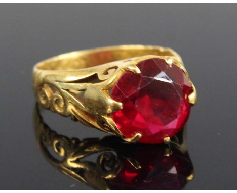 A yellow metal synthetic ruby single stone ring, comprising a round faceted synthetic ruby claw set within a scrollwork mount