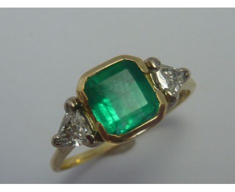 AN 18CT GOLD EMERALD AND DIAMOND RING, the step-cut emerald with triangular shape diamonds flanking the central emerald to th