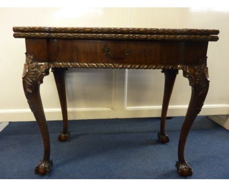 A MID VICTORIAN MAHOGANY FOLD-OVER CARD TABLE, the revolving top inlaid with baize and having counter recesses, the edge carv