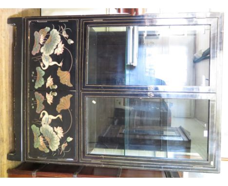 An Oriental black lacquered display cabinet, the twin glazed doors over a pair of doors depicting cranes, on bracket feet, 10