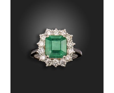 An emerald and diamond cluster ring, the emerald-cut emerald weighs approximately 3.40cts, set within a surround of round bri