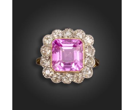 A synthetic sapphire and diamond cluster ring, the emerald-cut synthetic pink sapphire is set within a surround of old circul