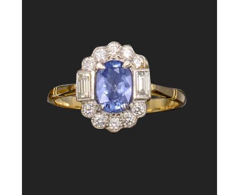 A sapphire and diamond cluster ring, the oval-shaped sapphire set within a surround of round brilliant-cut diamonds, with a b