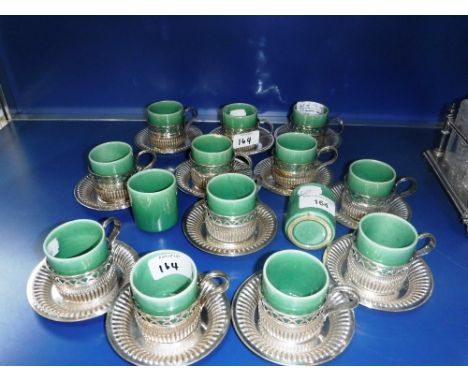 A SET OF TWELVE WHITE METAL CUP HOLDERS and saucers (STAMPED '800') with 14 green glazed cups