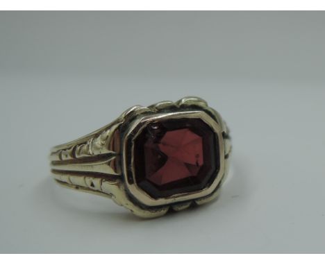 A yellow metal signet ring having a garnet style panel in collared mount to moulded shoulders on yellow metal loop, no marks,
