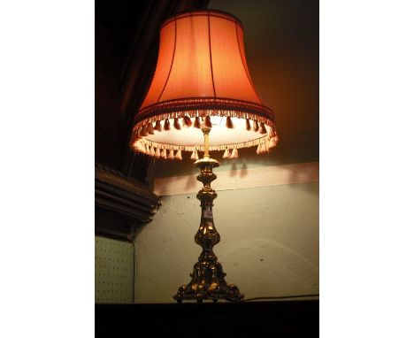 A brass table lamp, the rococo-style column supporting a pink tasselled shade.