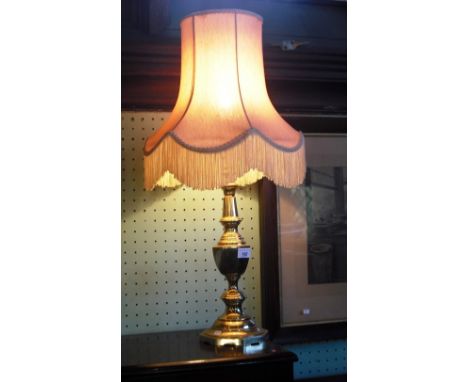 A brass table lamp, the turned knopped column supporting a fringed pink shade.