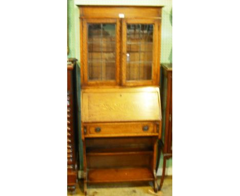 A circa 1920's oak bureau bookcase of small proportions, having plain cornice over a pair of leaded glazed doors, enclosing s