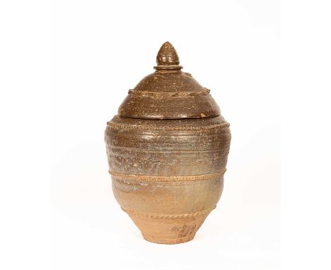 A stoneware lidded jar, possibly Khmer, the domed cover with finial, the jar with bands of ridged decoration and incised scri