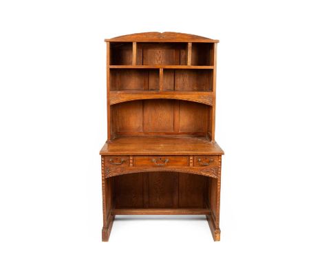 An Arts &amp; Crafts style oak bookcase and desk with a shelved superstructure and an arched cornice and with an arched desk 