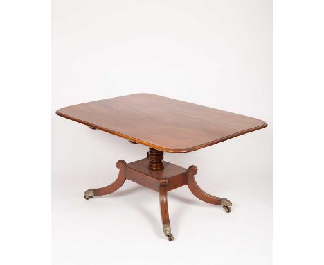 A Regency mahogany tilt top breakfast table, the oblong top on a turned column, the four scroll legs with lion mask caps and 