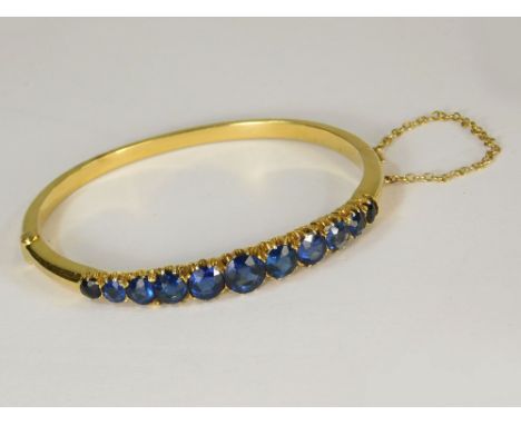 BANGLE. A late 19th/early 20th century unstamped yellow metal bangle, set a graduated row of blue paste stones.