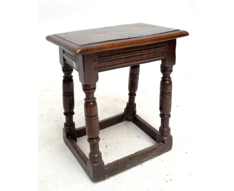 An 18th century oak joint stool with panelled top, linear decorated frieze and raised on ring turned and block supports unite