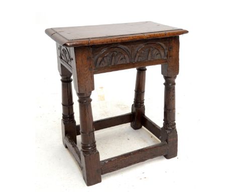 An 18th century oak joint stool with panelled top, carved frieze and ring turned and block legs united by stretchers, width 4