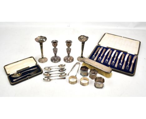 A quantity of silver including napkin rings, a pair of candlesticks, lace back teaspoons, sugar tongs, cased silver sheath ha