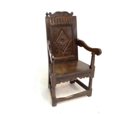 An early 18th century oak Wainscot chair with carved shaped top rail above lozenge decorated panelled back, swept arms, plank