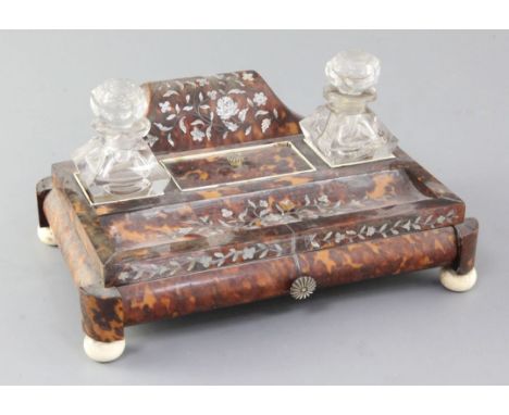 An early Victorian mother of pearl inset tortoiseshell ink stand, with two cut glass wells and frieze drawer, on ivory ball f