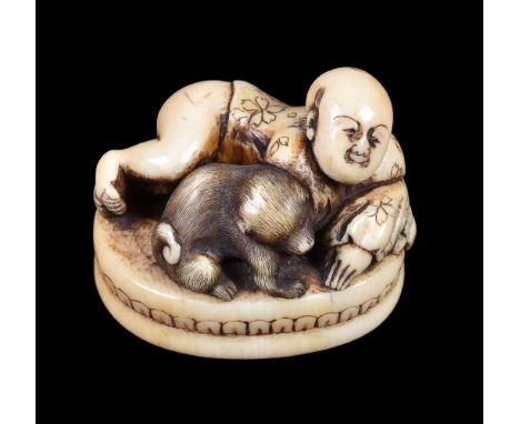 ϒ A Japanese Ivory Seal Netsuke of oval form, depicting a semi-naked boy reclining on an oval base with his dog, the bottom c