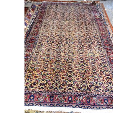 A Mashhad carpet, Persian, the pale fawn field with an allover herate design; a burgundy rosette, boteh and floral vine borde