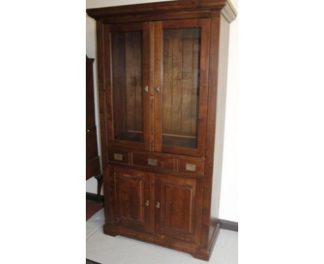 A modern hardwood display cabinet, the overhanging cornice raised above two glazed doors above three frieze drawers with flus