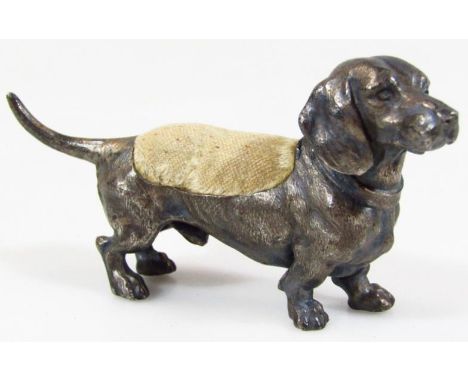 A cold painted metal dachshund dog pin cushion, in standing pose, unmarked, probably early 20thC, 20cm wide.