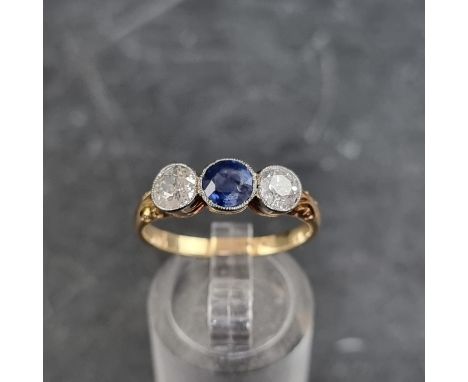 A yellow metal three stone ring,&nbsp;set central mixed cut sapphire with an old cut diamond to each side,&nbsp;stamped '18ct