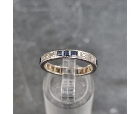 A white metal eternity ring, set twelve calibre sapphires and twelve small diamonds, size N. 