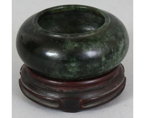 A SMALL CHINESE SPINACH GREEN JADE WATER POT, together with a fitted wood stand, the stone of predominantly dark tone with li