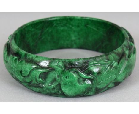 A CHINESE JADE BANGLE, carved to the rounded rim with foliage, the green stone with black inclusions, 3in diameter, the inner