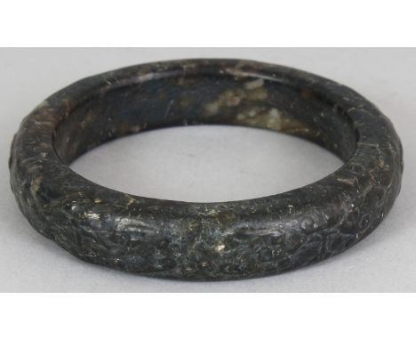 A CHINESE JADE BANGLE, carved to the rounded rim with archaic designs, the predominantly black stone with pale inclusions, 3.