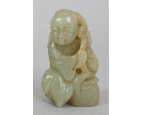 A CHINESE CELADON JADE FIGURE OF A BOY, seated next to a basket and supporting a fish on a leafy frond, 2.25in high.