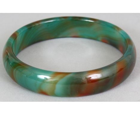 A CHINESE JADE LIKE GLASS BANGLE, of striated green and russet colouring, 3in diameter, the inner rim 2.5in diameter.