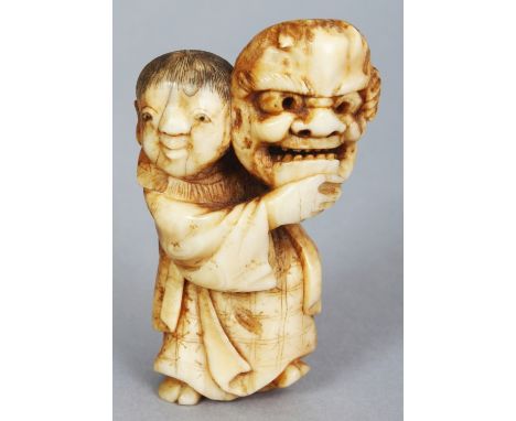 A JAPANESE MEIJI PERIOD IVORY NETSUKE OF A STANDING BOY, unsigned, the boy bearing aloft a Noh mask, the details engraved and