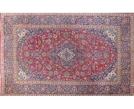 A Kashan carpet with central floral medallion, on a red &amp; blue ground, contained by floral borders, 304 x 199cm 