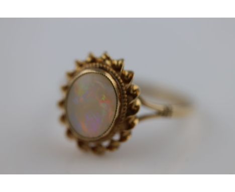 A white precious opal 9ct yellow gold ring, the central oval cabochon cut opal measuring approximately 9mm by 7mm, displaying