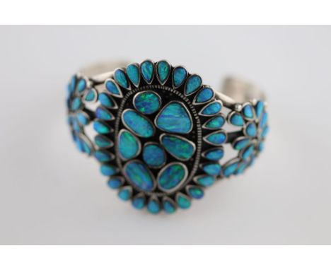 A black opal and silver cluster bangle, the centre oval cluster with eight rub over set oval and irregular oval cabochon cut 