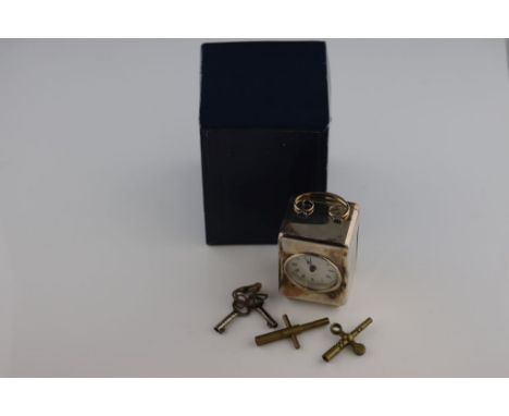 A silver travel clock in the form of a carriage clock, raised on four ball feet, white enamel dial with black Roman numerals 