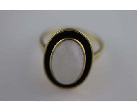 A precious white opal and black enamel unmarked yellow gold ring, the centre oval cabochon cut opal measuring approximately 1