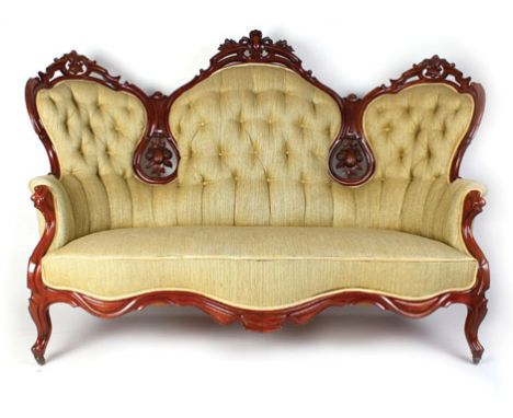 A 19th century mahogany framed and button upholstered parlour sofa, the tri-form back surmounted by foliate and armorial carv