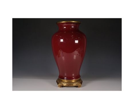 Elegant porcelain vase featuring a deep sang de boeuf glaze, enhanced by intricate gilt bronze mounts at the rim and base. Th